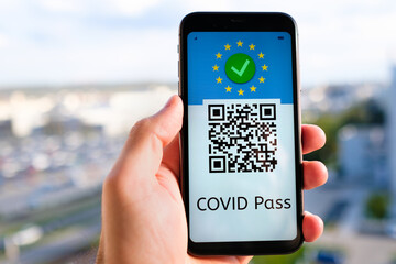 Covid pass with QR code on the screen in smartphone in mans hand on the background of cityscape