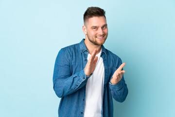 Russian handsome man isolated on blue background applauding after presentation in a conference