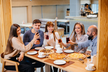 A group of young cheerful friends is sitting in a cafe talking and eating pizza. Lunch at the pizzeria.