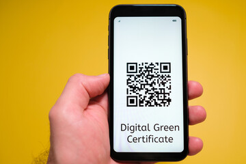 Digital Green Certificate with QR code on the screen of mobile phone in mans hand on the yellow background