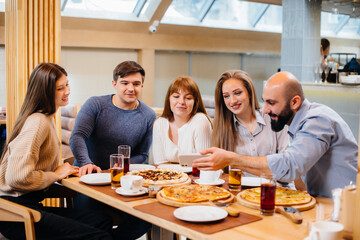 A group of young cheerful friends is sitting in a cafe talking and eating pizza. Lunch at the pizzeria.