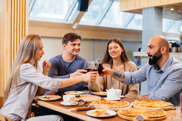 A group of young cheerful friends is sitting in a cafe talking and eating pizza. Lunch at the pizzeria.