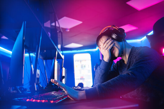 Streamer young man facepalm professional gamer playing online games computer with headphones, neon color