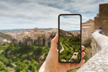 Horizontal view of unrecognizable woman taking a picture with her phone of a travel destination in Europe. Technology, tourism and holidays concept in the spanish city of Cuenca.
