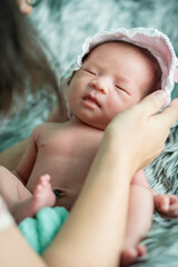 A newborn baby wrapped in a green cloth with hat was placed on a gray fluffy rug. She was making a cheerful expression, smiling, bright jam. soft focus.