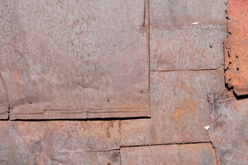 A fragment of the wall of an old building, sheathed with rusty steel sheets. The joints of the sheets are uneven, the edges are partially destroyed. Background. Texture.