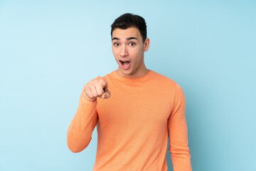 Young caucasian handsome man isolated on blue background surprised and pointing front