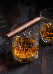 Single malt scotch whiskey in crystal glasses with cuban cigar on wooden background