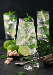 Glasses of Mojito cocktail with ice cubes,mint and lime on black board with spoon and fresh limes with cane sugar.
