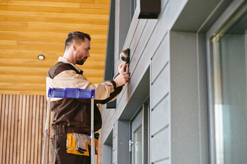 Young man in uniform fixing alarm system on wall above the door inside house