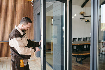 Young man in uniform using handtool while repairing door of large modern house