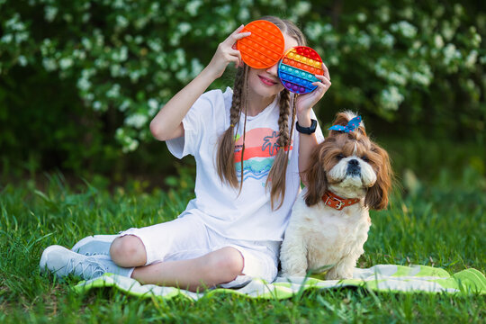 Creative Image With Child Playing Poppit Fidget Toy. Young Girl At  Holding Pop It New Fidget Toy, Popular With Kids, Helps Them To Concentrate. Girl on the lawn with a dog playing antistress