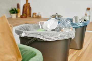 A plastic bag with used disposable kitchenware and other waste in trash bin on wooden table