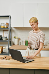 A person using laptop by kitchen table against shelves and cabinets