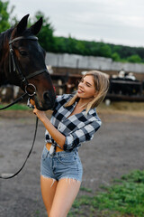 Obraz premium A young pretty girl rider poses near a thoroughbred stallion on a ranch. Horse riding, horse racing