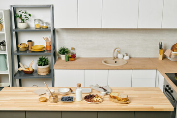 Fototapeta na wymiar Large modern kitchen with kitchenware on shelves, white cabinets on walls, food and milk on wooden table