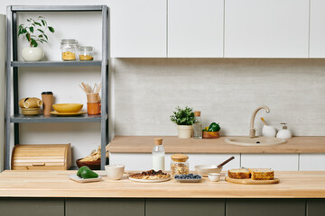 A large modern kitchen with a shelf full of kitchenware and wooden table with food