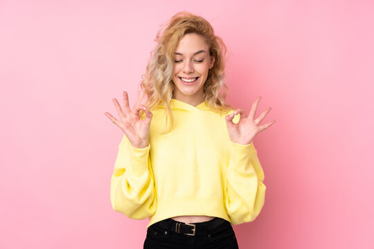 Young blonde woman wearing a sweatshirt isolated on pink background in zen pose