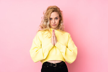 Young blonde woman wearing a sweatshirt isolated on pink background keeps palm together. Person asks for something