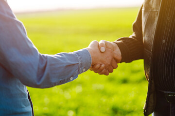 Handshake two farmer after agreement.  Two farmer standing and shaking hands in a  green wheat field. The concept of the agricultural business. Negotiations. - obrazy, fototapety, plakaty