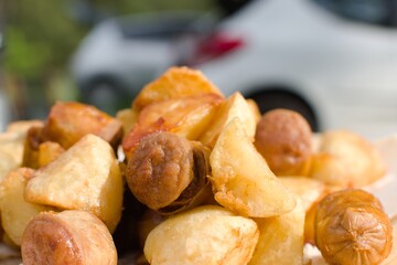 camping food. appetizing fried potatoes and sausages on table on blurred background. focus on foreground