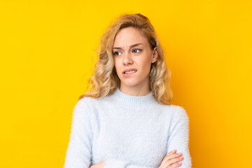 Young blonde woman isolated on yellow background with confuse face expression