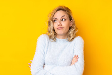 Young blonde woman isolated on yellow background making doubts gesture while lifting the shoulders