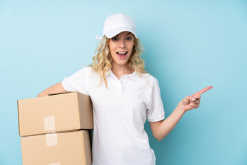 Young delivery woman isolated on blue background surprised and pointing finger to the side