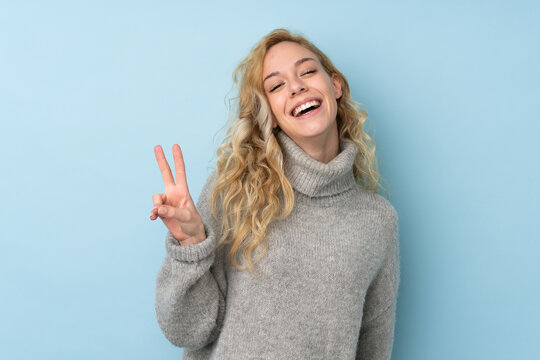 Young blonde woman wearing a sweater isolated on blue background smiling and showing victory sign