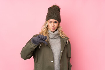 Young girl with winter hat isolated on pink background showing thumb down sign