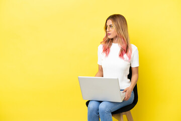 Naklejka premium Young woman sitting on a chair with laptop over isolated yellow background looking to the side