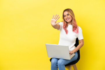Young woman sitting on a chair with laptop over isolated yellow background counting five with fingers