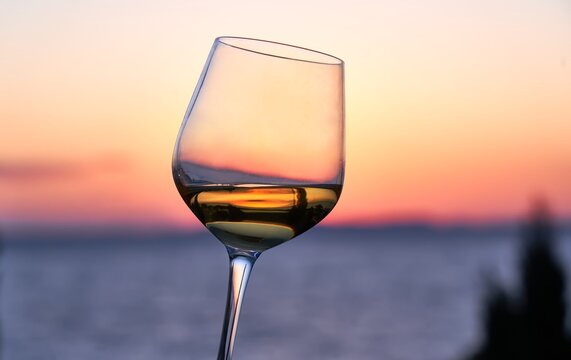 Close up image of glass of wine in woman's hand with the sea and sunset in the background. Summer holiday, vacation concept.
