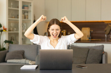 Excited happy caucasian woman sitting at the table at home feel euphoric win online lottery or get...
