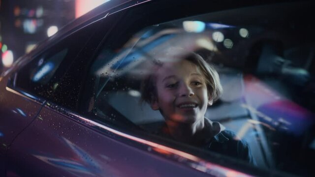 Excited Young Boy is Sitting on Backseat of a Car, Commuting Home at Night. Looking Out of the Window with Amazement of How Beautiful is the City Street with Working Neon Signs. Cinematic Footage.