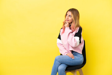 Young woman sitting on a chair over isolated yellow background having doubts