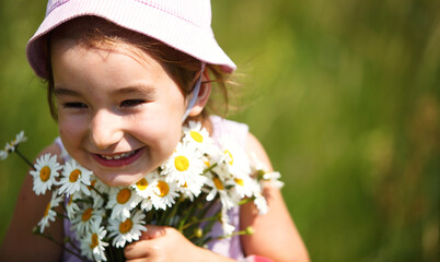 Little girl with a bouquet of daisies in summer on a natural background. Happy child,panama hat for sun protection. International Children's Day. Copy space. Authenticity, rural life, eco-friendly