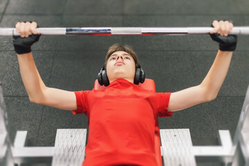 young man with headphones in the gym does barbell press, teenager leads healthy lifestyle working out in the gym
