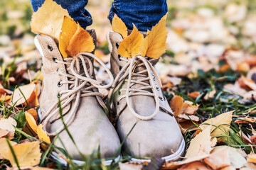 women's legs in jeans and autumn boots on yellow foliage, close-up