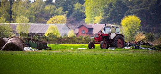An old, abandoned farm tractor standing against a background of distant farm buildings. Blurred...