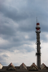 Fototapeta premium Rooftop of industrial halls and an inactive municipal heating plant chimney converted into a mast for telecommunications antennas against the cloudy sky. The photo was taken in natural daylight.