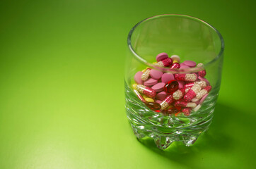 pharmaceutical technologies. dietary supplements. colorful pills are in a glass cup on a green background.