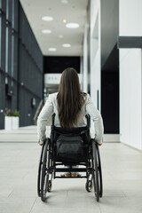 Vertical back view portrait of young businesswoman in wheelchair entering office building