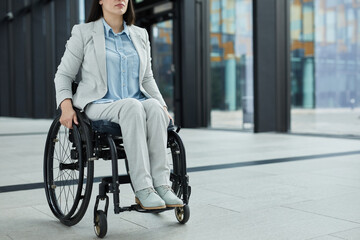 Cropped portrait of successful young businesswoman in wheelchair in graphic office lobby interior,...