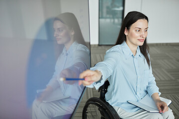 High angle portrait of successful young woman in wheelchair leading business meeting with team and...