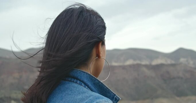 Close back view of  woman hair tender movement in the air in slow motion.  Woman in jeans jacket  walking on sandy beach