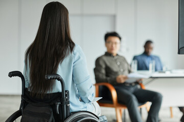 Back view portrait of young woman in wheelchair talking to diverse business team during group discussion in office, copy space