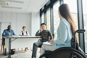 Side view portrait of young woman in wheelchair giving speech to diverse business team in office, copy space