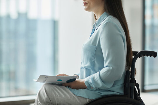 Cropped side view portrait of young businesswoman in wheelchair holding booklet while giving speech or attending conference, copy space