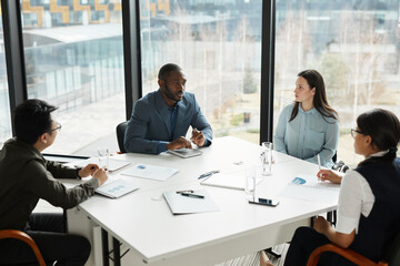 High angle view at diverse business team discussing project at meeting table in modern office with focus on young woman in wheelchair listening to colleagues